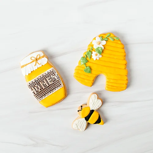 What to make - Cookies Bright yellow bee-shaped sugar cookies decorated with floral accents, honey jar, and bee design, perfect for cake decorating and bakery supplies from Over the Top Cake Supplies.