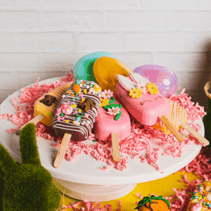 Colorful spring-themed cake pops with vibrant decorations on a white cake stand, perfect for festive celebrations and birthday parties.