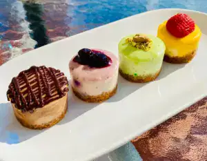 Delicious mini cheesecakes with chocolate, berry, pistachio, and strawberry toppings, perfect for dessert or special occasions from Over the Top Cake Supplies.