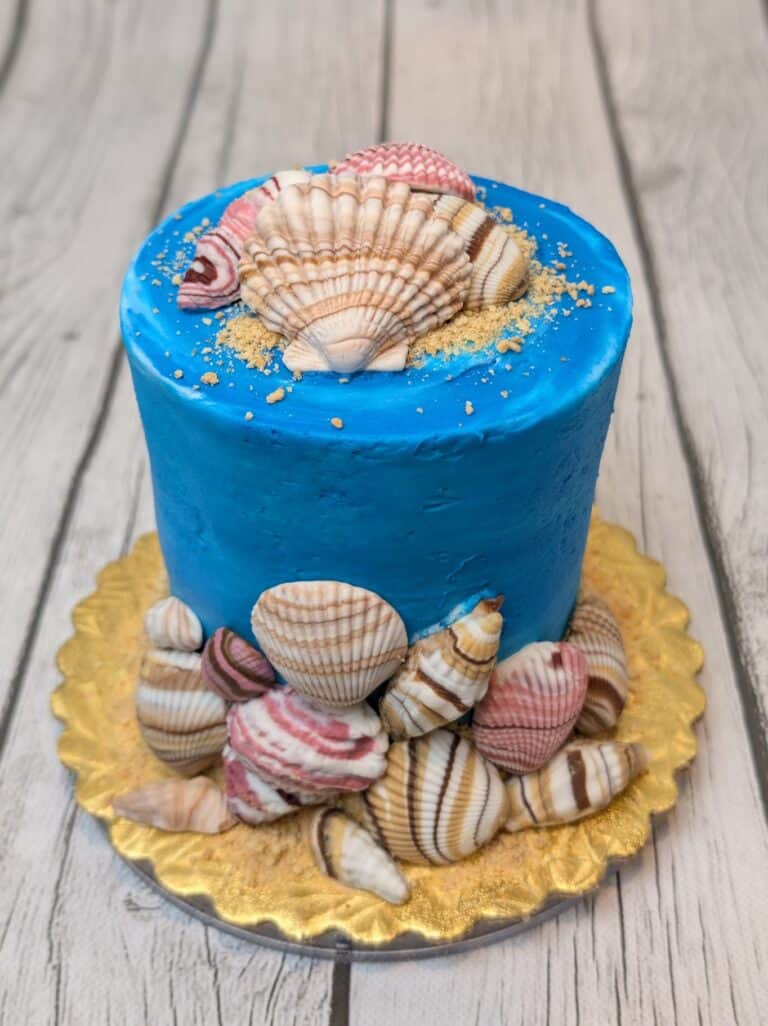 beach vibes cake Blue cake with seashell decorations on gold platter.