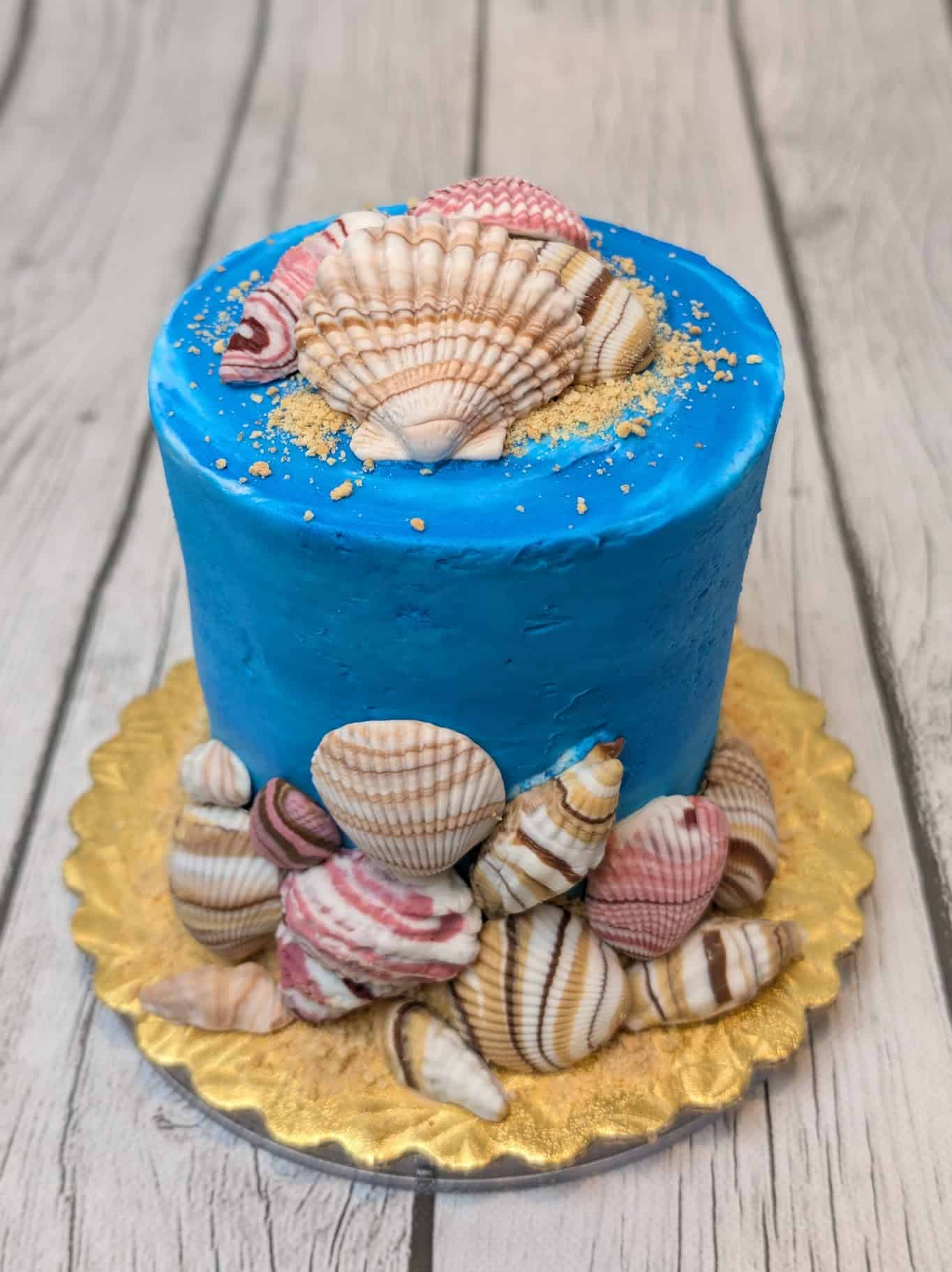 Blue cake with seashell decorations on gold platter.