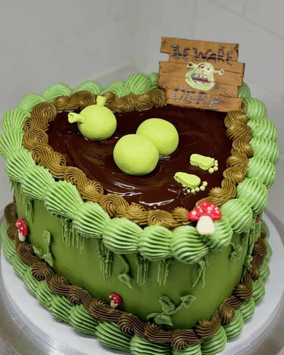 Shrek-themed cake with green apples and sign.