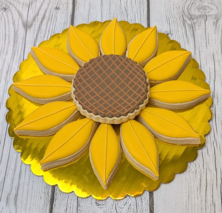 sunflower cookie platter Bright yellow sunflower-shaped cookies with a waffle-patterned cookie at the center, displayed on a gold cake board, perfect for cake decorating and custom cookie designs.
