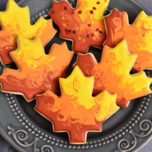 Vibrant maple leaf cookies decorated with colorful autumn-inspired icing for fall celebrations and Thanksgiving desserts. Perfect for baking and decorating with cake supply products.