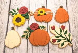 Soft pumpkin-shaped cookies decorated with autumn floral and harvest motifs, perfect for fall celebrations and seasonal cake decorating supplies.