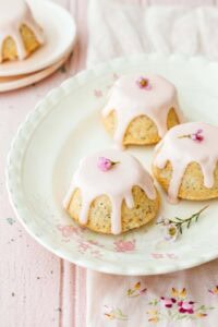 Delicious vanilla cupcakes with pink glaze and floral garnishes on a vintage floral plate, perfect for cake decorating and baking supplies.