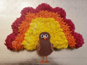 Colorful flower cupcake rainbow with turkey decoration for Thanksgiving cake topper, decorated with vibrant buttercream blooms and a cute edible turkey figure, perfect for festive celebrations.