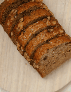 Moist banana nut bread topped with chopped walnuts, served on a wooden surface. Perfect for baking supplies and decorating with cake tools from Over the Top Cake Supplies.