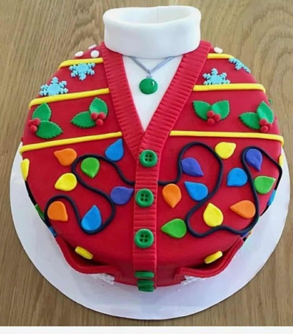 Festive Christmas sweater cake decorated with colorful fondant lights, holly leaves, and buttons, perfect for holiday celebrations - Over the Top Cake Supplies.