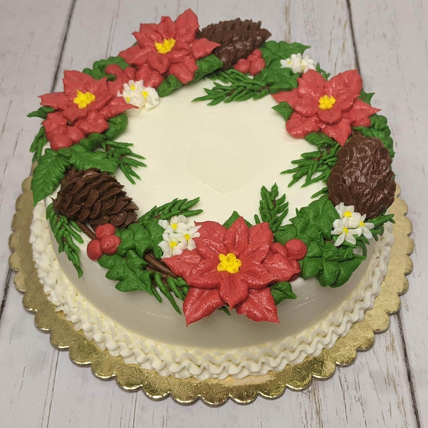 Decorative holiday cake with poinsettia flowers, pinecones, and greenery for Christmas celebrations.