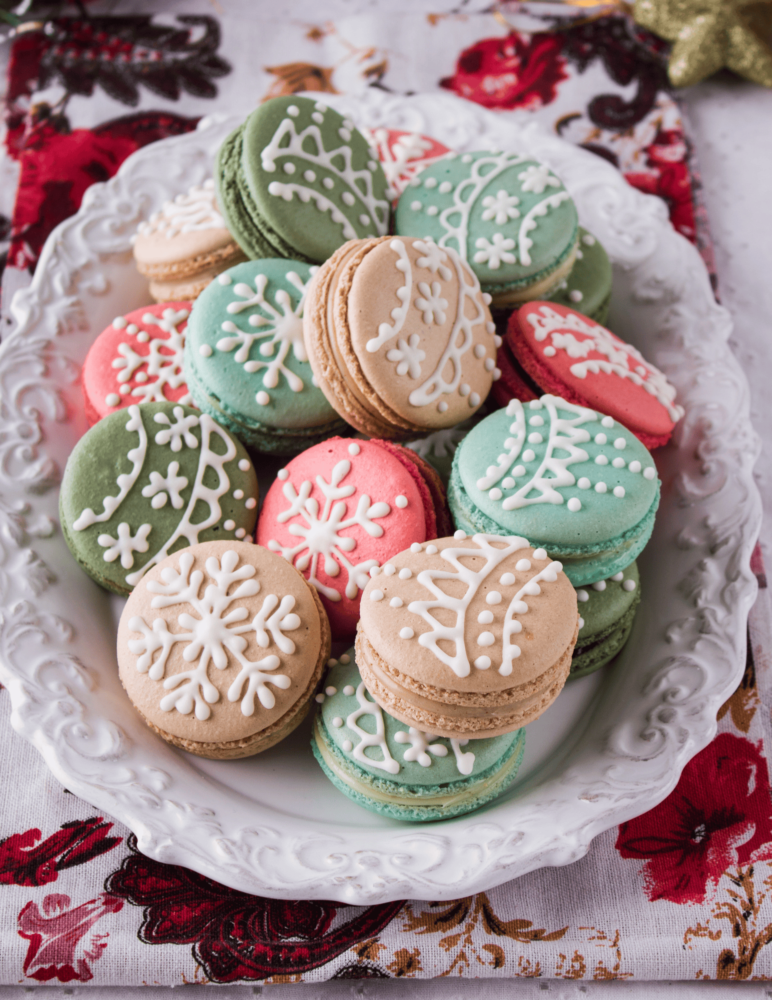 Colorful Christmas macarons decorated with white icing on a decorative white platter, ideal for holiday baking supplies and cake decorating.