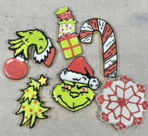 Colorful Christmas themed decorated cookies featuring Grinch, candy cane, snowflake, Christmas tree, presents, and Santa hat designs from Over the Top Cake Supplies. Perfect for holiday treats and baking supplies.