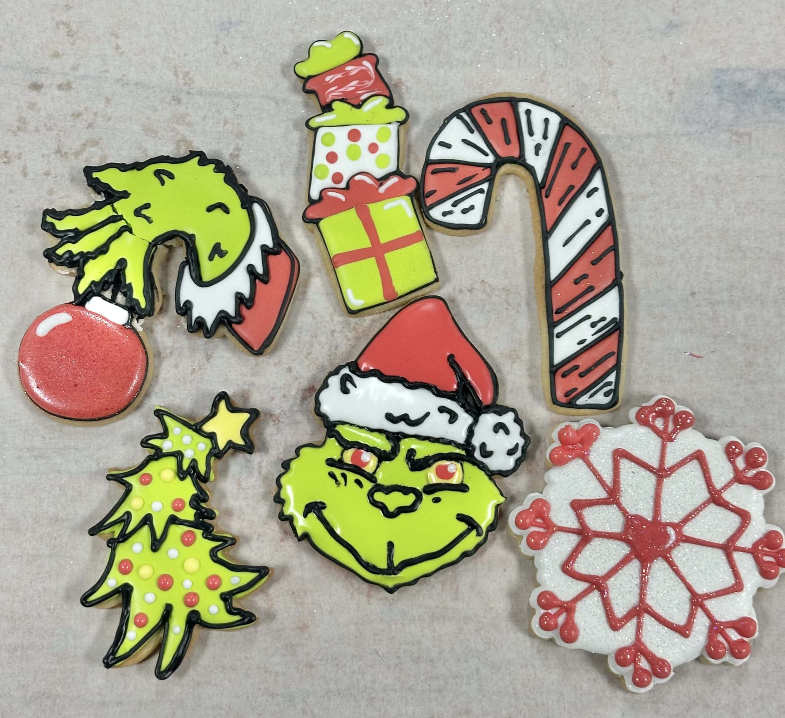 Colorful Christmas themed decorated cookies featuring Grinch, candy cane, snowflake, Christmas tree, presents, and Santa hat designs from Over the Top Cake Supplies. Perfect for holiday treats and baking supplies.