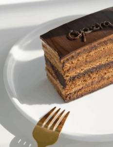 Delicious layered chocolate cake on a white plate, featuring rich chocolate ganache and intricate frosting, perfect for cake decorating and baking supplies from Over the Top Cake Supplies.