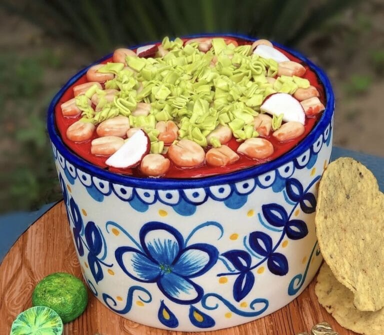 pozole cake Chocolate cake with colorful fruit and green shredded topping, decorated in a vibrant blue and white floral cake stand, perfect for birthday celebrations or special events.