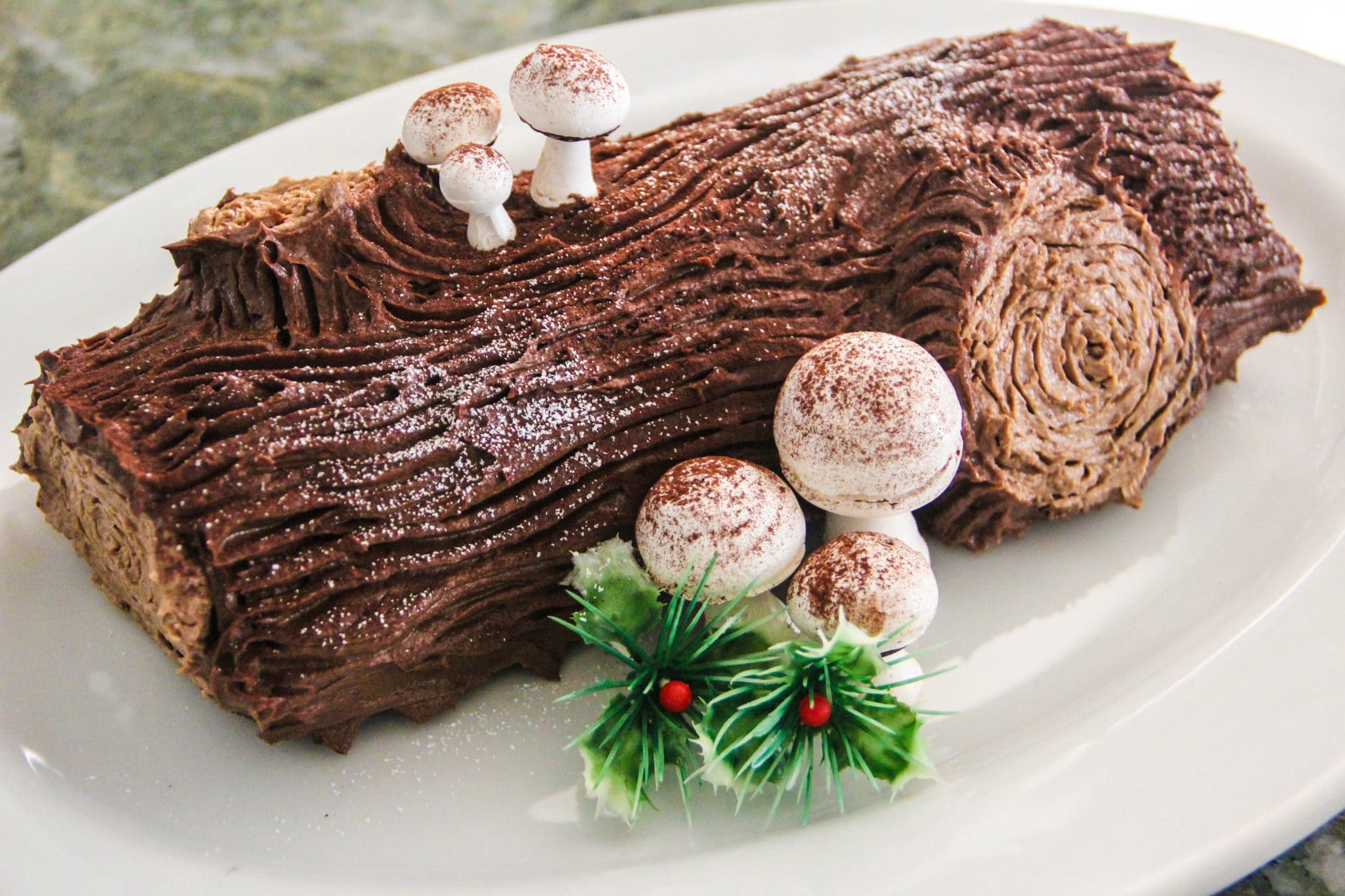Chocolate yule log cake for holiday desserts, decorated with edible mushrooms and holly leaves, perfect for Christmas celebrations. Fancy cake, cake supplies, and holiday baking ideas.