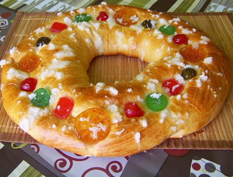 roscon reyes Colorful fruit cake wreath with gummy candies and powdered sugar topping on a bamboo mat. Perfect for celebrating special occasions with vibrant, sweet decorations and bakery-quality presentation.