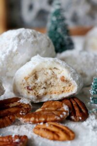Cream-filled Christmas snowball cookies with pecans, powdered sugar, and holiday decorations for festive baking.