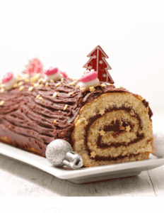 Decorated Christmas yule log cake with chocolate frosting, pink and white fondant accents, edible star sprinkles, and holiday-themed cake topper, on a white serving platter.
