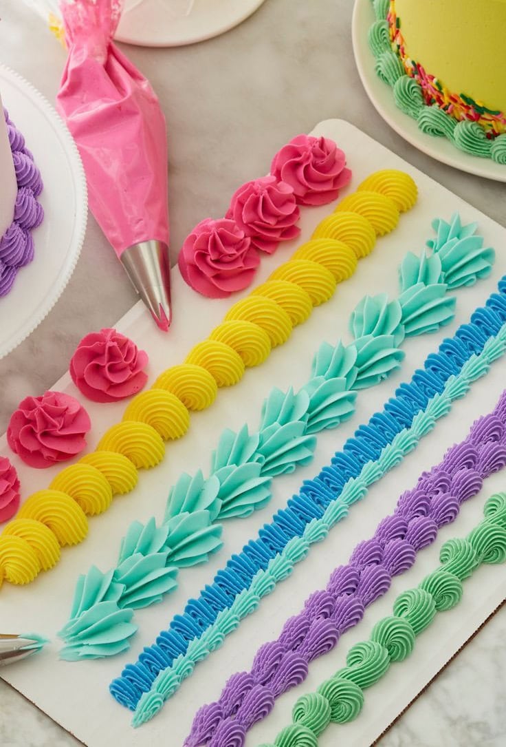 Bright, pastel-colored buttercream piping tips and techniques for cake decorating, showcasing vibrant frosting designs including rosettes, shells, and textured patterns.