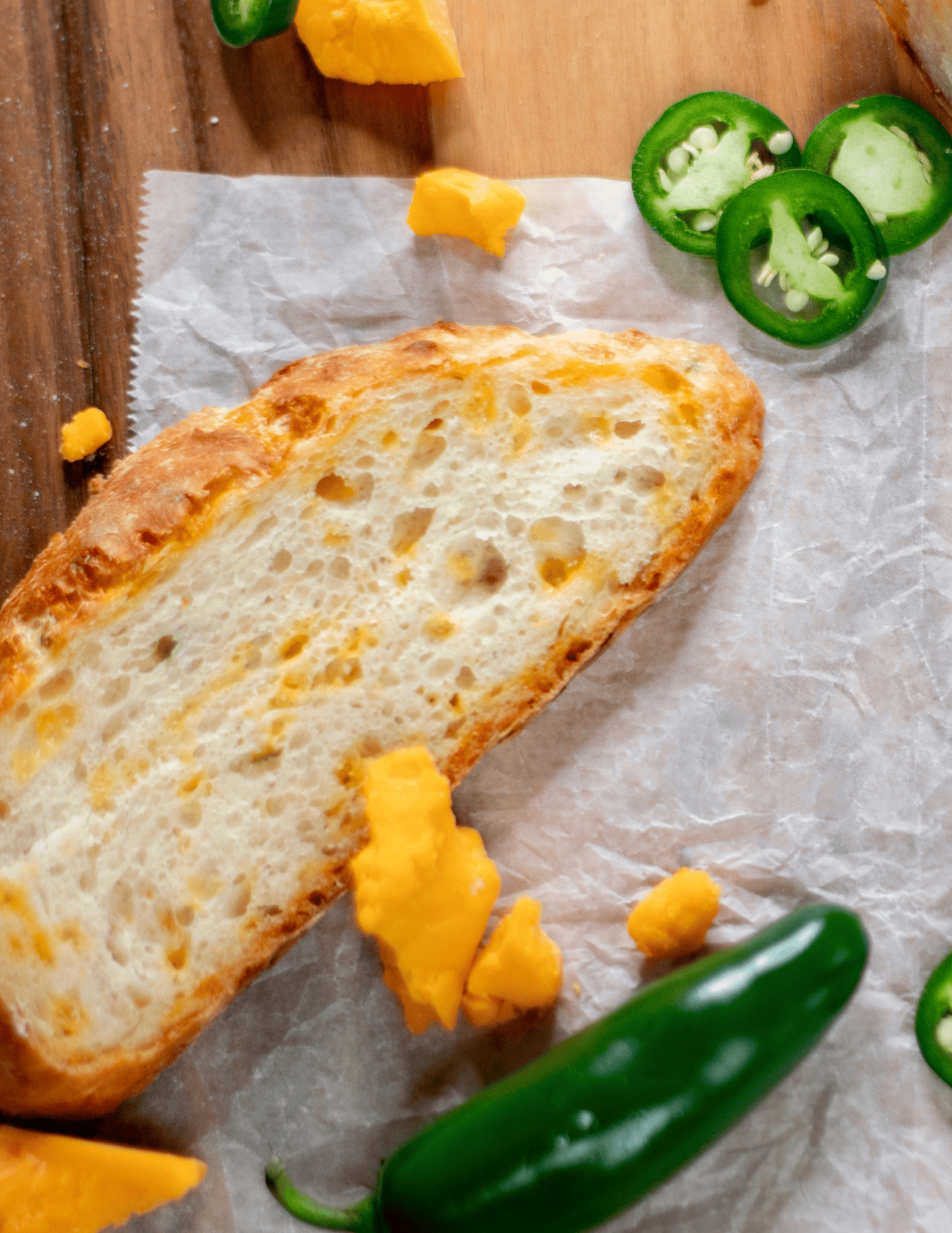 Freshly baked garlic bread with melted cheese, served on parchment paper with jalapeño slices and diced cheddar cheese, perfect for cake and baking enthusiasts.