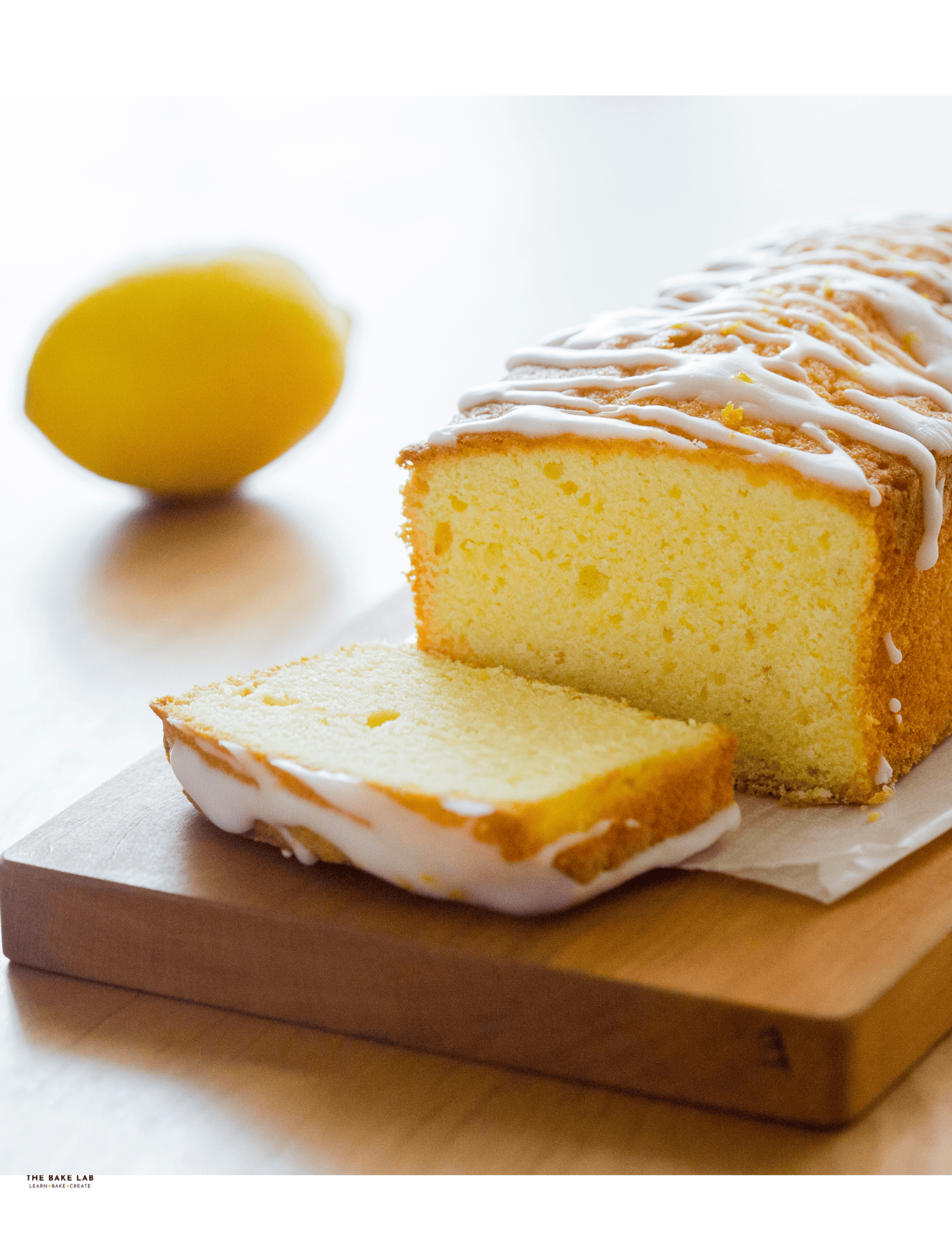Lemon cake loaf with lemon glaze on wooden board, fresh lemon in background, perfect for cake decorating and baking supplies.