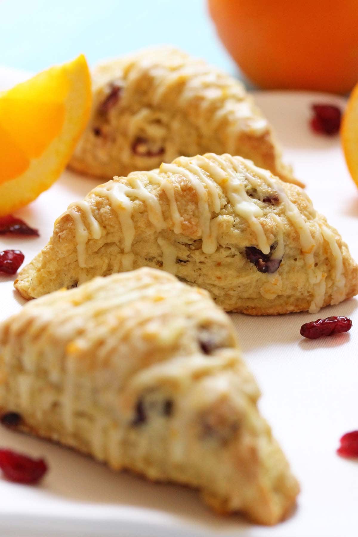 Freshly baked scones with white chocolate drizzle, dried cranberries, and orange slices on a white plate, perfect for baking supplies and dessert ingredients from Over the Top Cake Supplies.