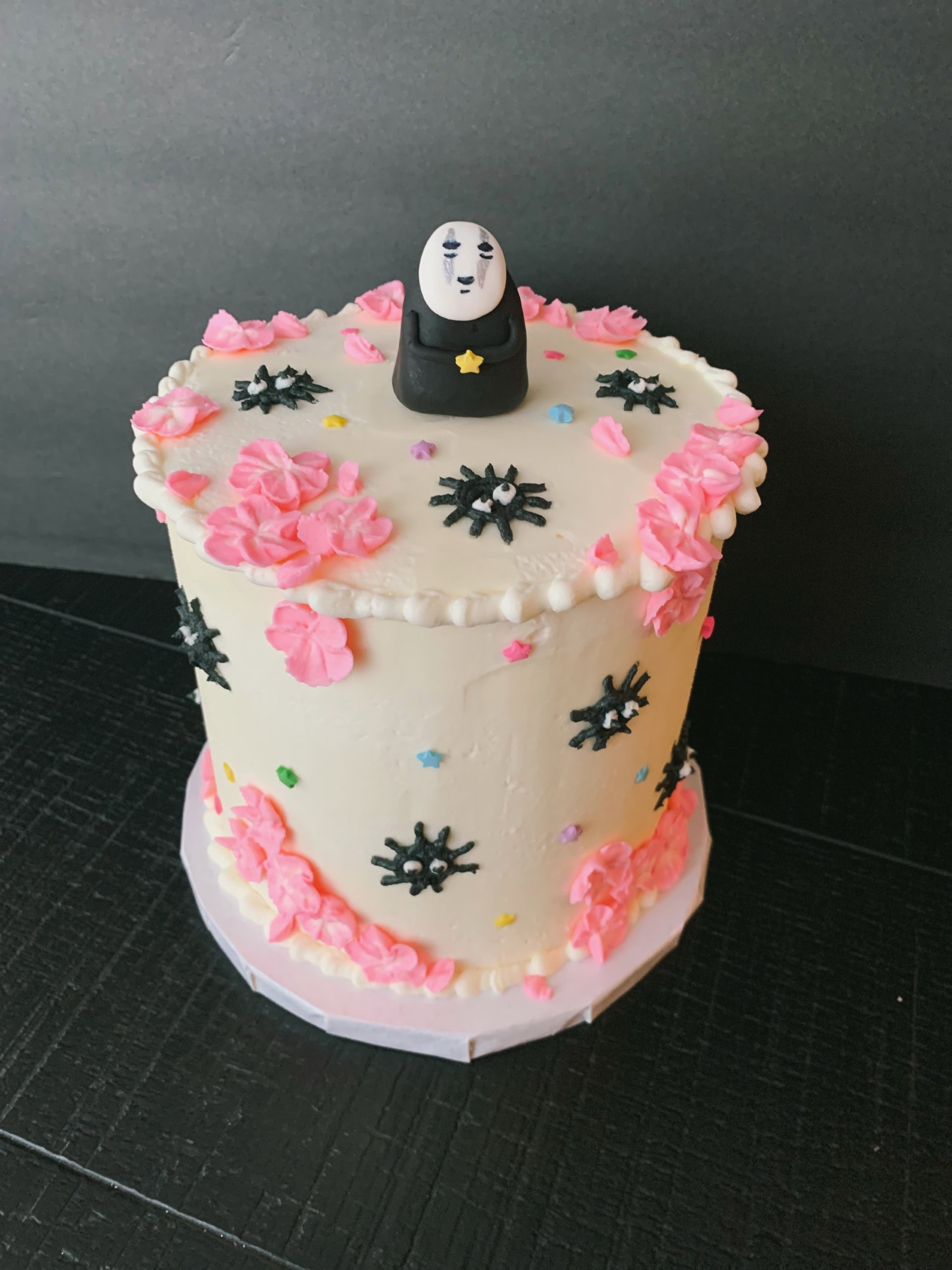 Decorative birthday cake with pink flower frosting and black snowflake-shaped accents, topped with a unique character cake topper, designed for celebrations.