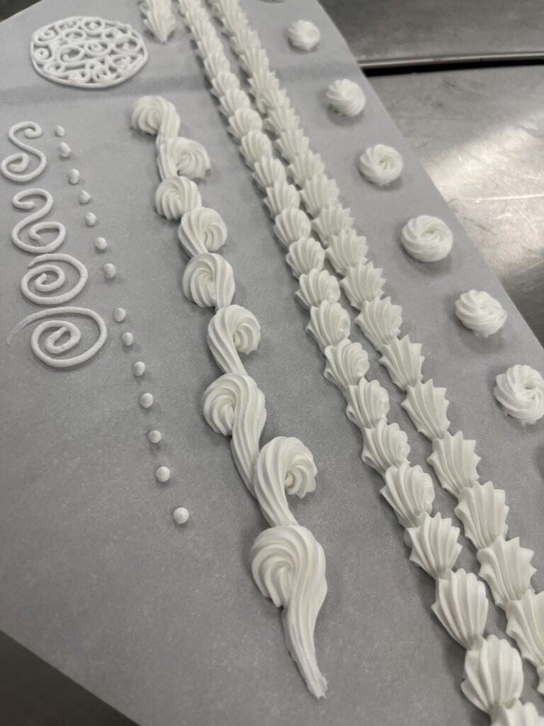 Delicate white piping gel and royal icing for cake decorating, showcasing intricate piping designs, shell motifs, and decorative borders for a professional cake finish.