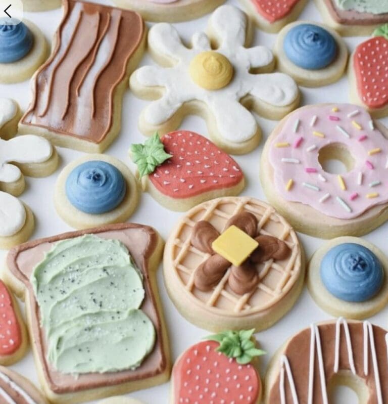 Colorful decorated sugar cookies with various icing designs, fruit shapes, and sprinkles, perfect for baking enthusiasts and party favors.