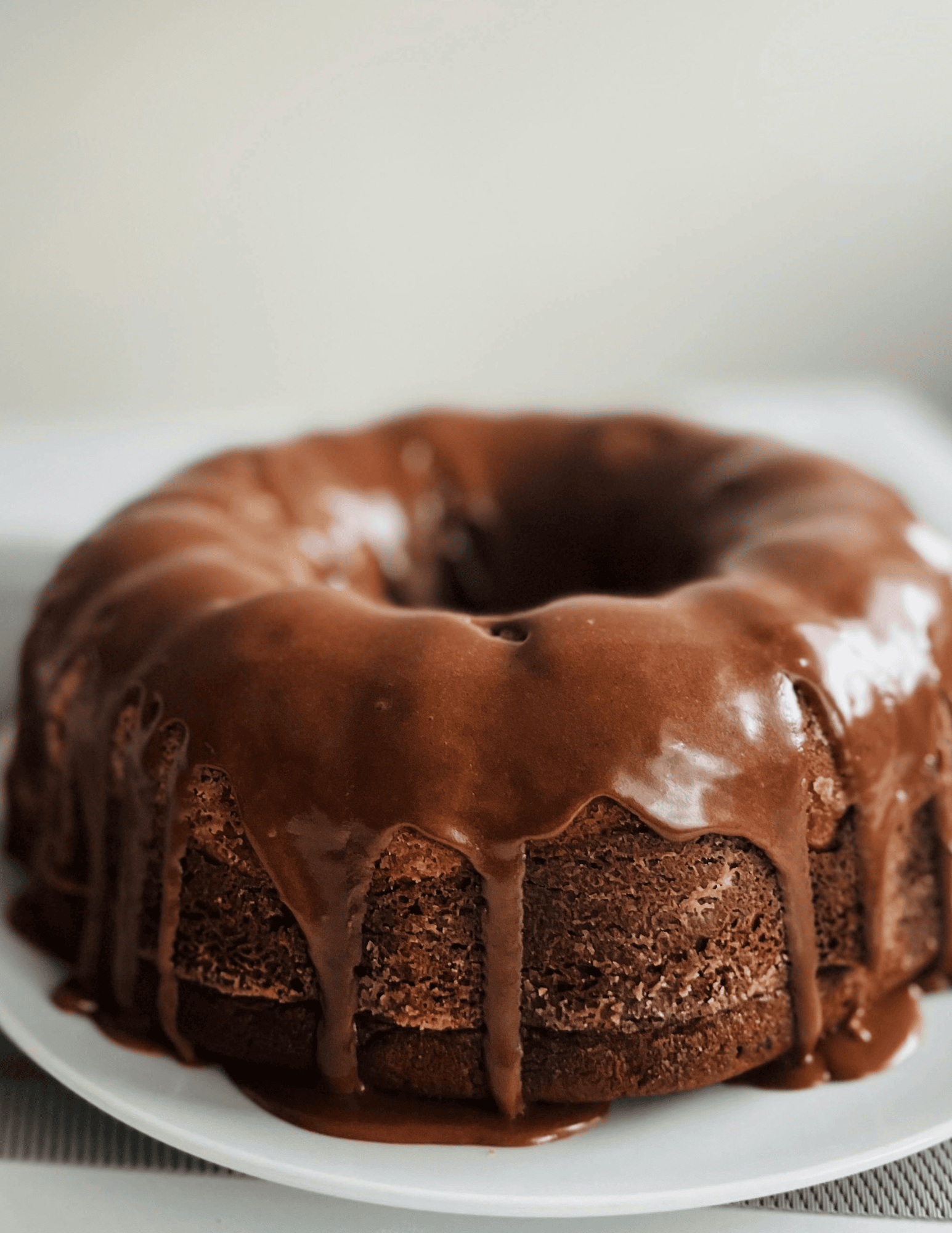 Rich chocolate cake with glossy chocolate ganache drip on a white plate, perfect for celebration desserts.
