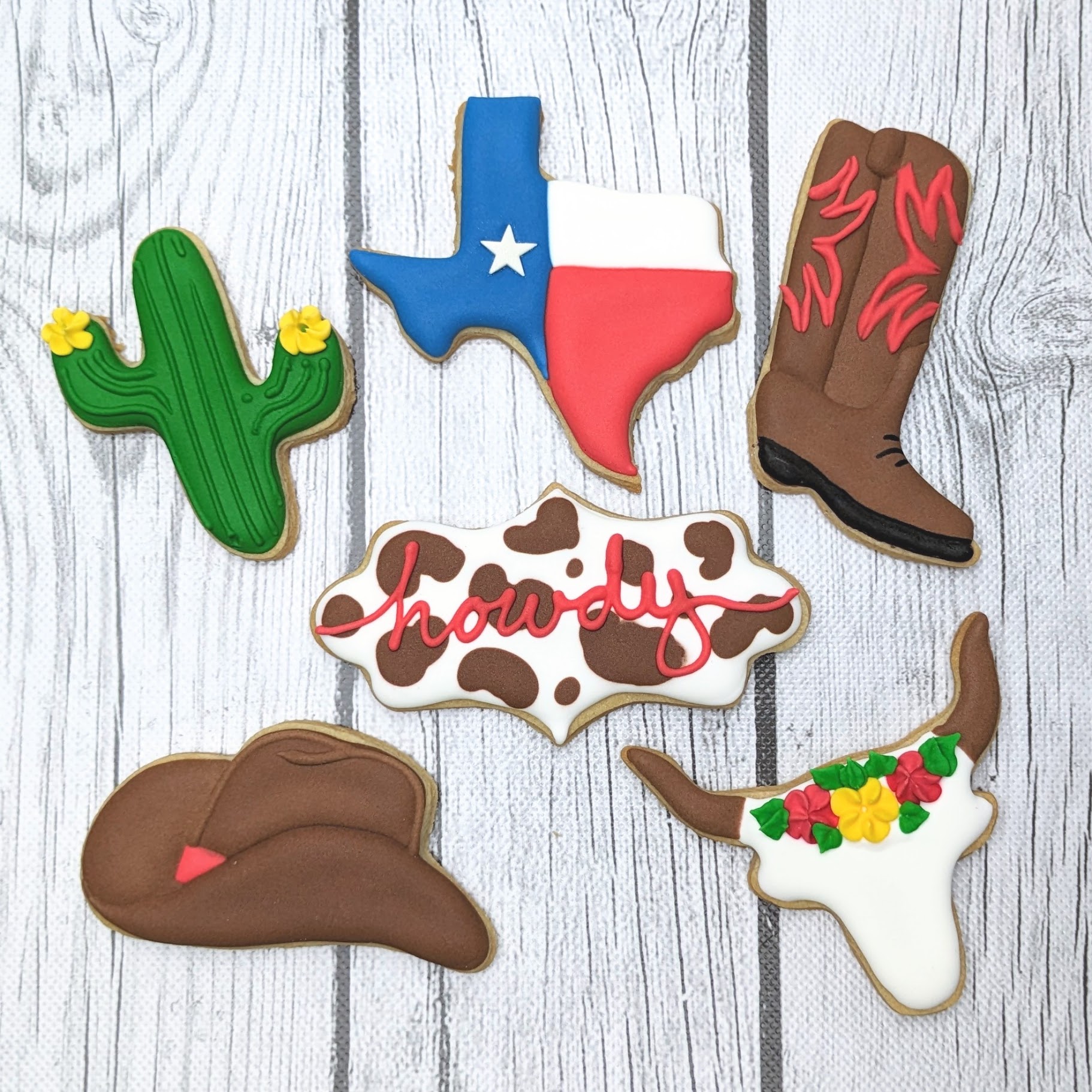 Colorful Texas-themed cookies featuring cowboy hats, cacti, a "Howdy" sign, and a cowboy boot, designed for Western and country party decor and celebrations. Each cookie is decorated with vibrant icing for a festive look.