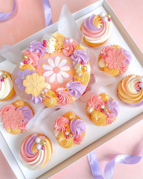 Spring Bento Box cake with pastel-colored floral and swirl cupcakes, decorated with pearls and edible flowers, perfect for celebrations. Delightful pastel floral and swirl cupcakes arranged in a spring-themed bento box, featuring pink, purple, and yellow hues with pearl accents and edible flowers, ideal for spring parties.