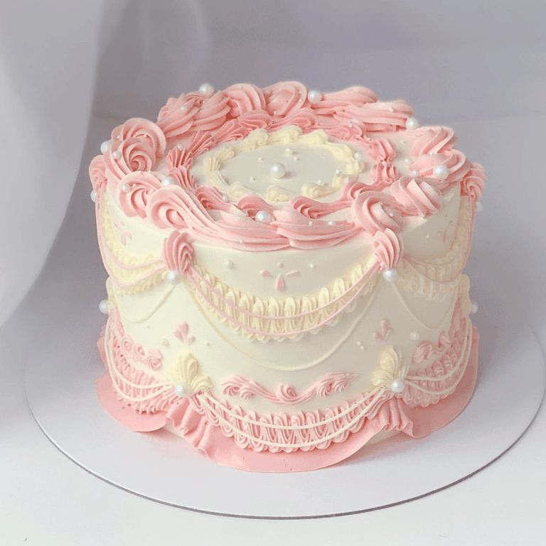 Elegant pastel vintage cake decorated with pink and white buttercream swirls, pearls, and intricate piping, perfect for cake decorating enthusiasts.