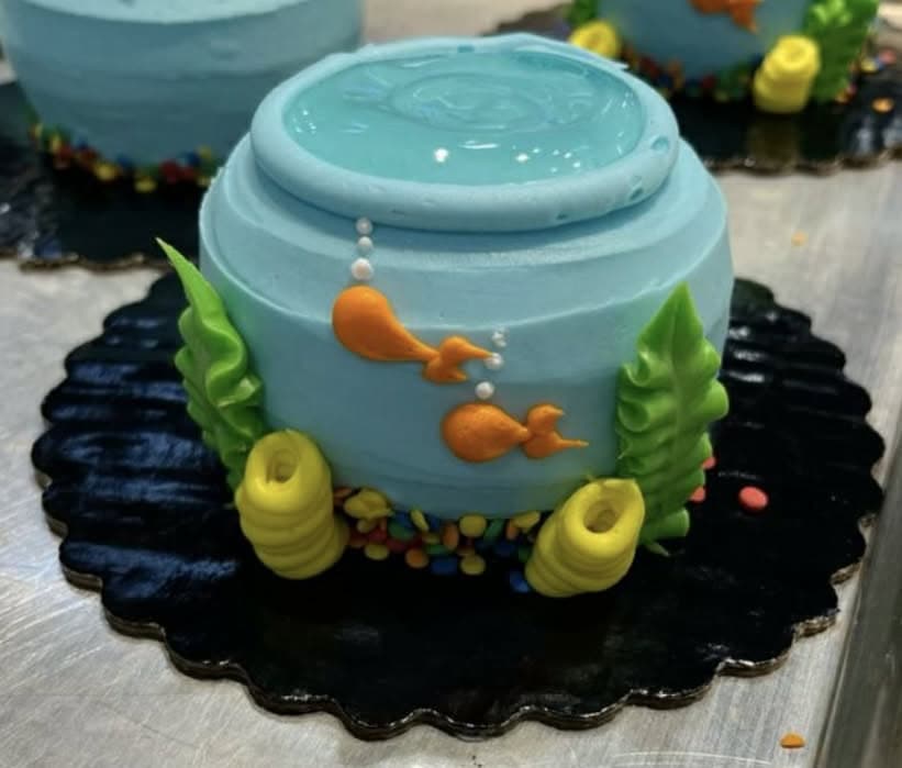 Colorful fish bowl cake decorated with orange fish and green seaweed, perfect for kids' baking classes and cake decorating supplies.