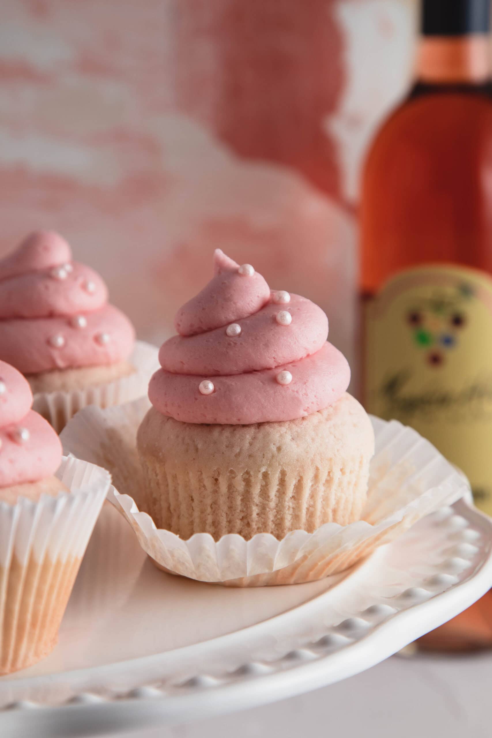Delicious wine-infused cupcakes topped with pink frosting and edible pearl decorations, perfect for elegant celebrations and wine lovers.