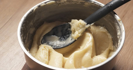 Close-up of smooth, creamy pâte à choux dough in a mixing bowl with a spatula, ready for baking, ideal for pastry chefs and baking enthusiasts.