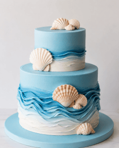 Beautiful two-tier blue ocean-inspired cake decorated with realistic seashells, perfect for beach-themed celebrations or special occasions.