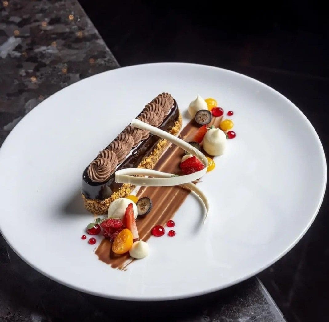 Delicious chocolate dessert decorated with fresh strawberries, raspberries, and colorful fruit accents on a white plate. Perfect for cake decorating and pastry art enthusiasts.