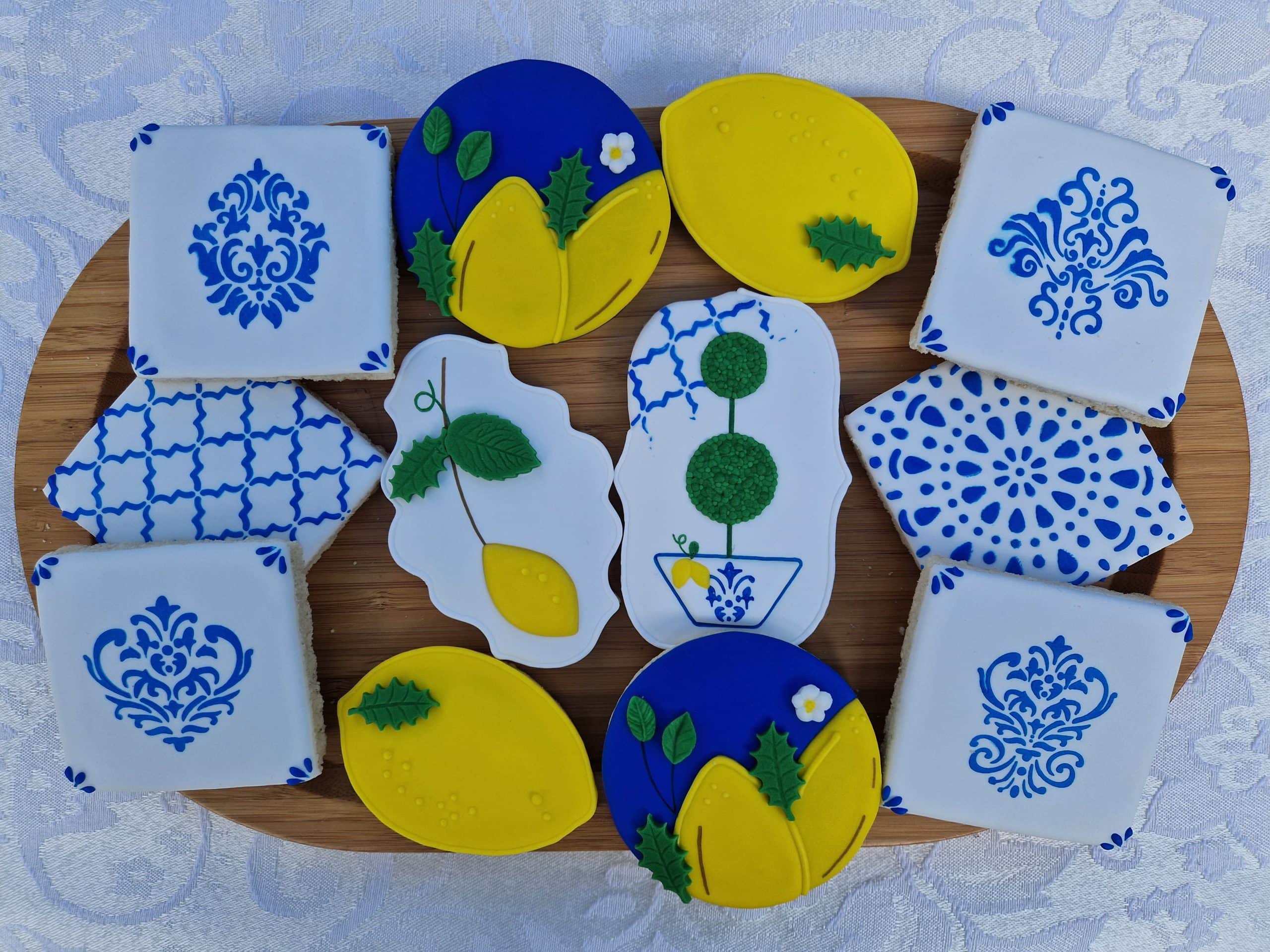 Assorted lemon-shaped and floral-patterned cookies in yellow, blue, and white, arranged on a wooden tray, perfect for cake decorating and dessert table displays.