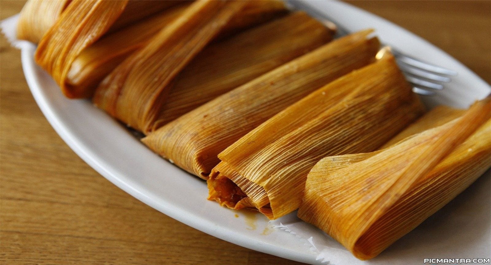 Close-up of freshly cooked tamales wrapped in corn husks on a white plate, highlighting their texture and traditional presentation.