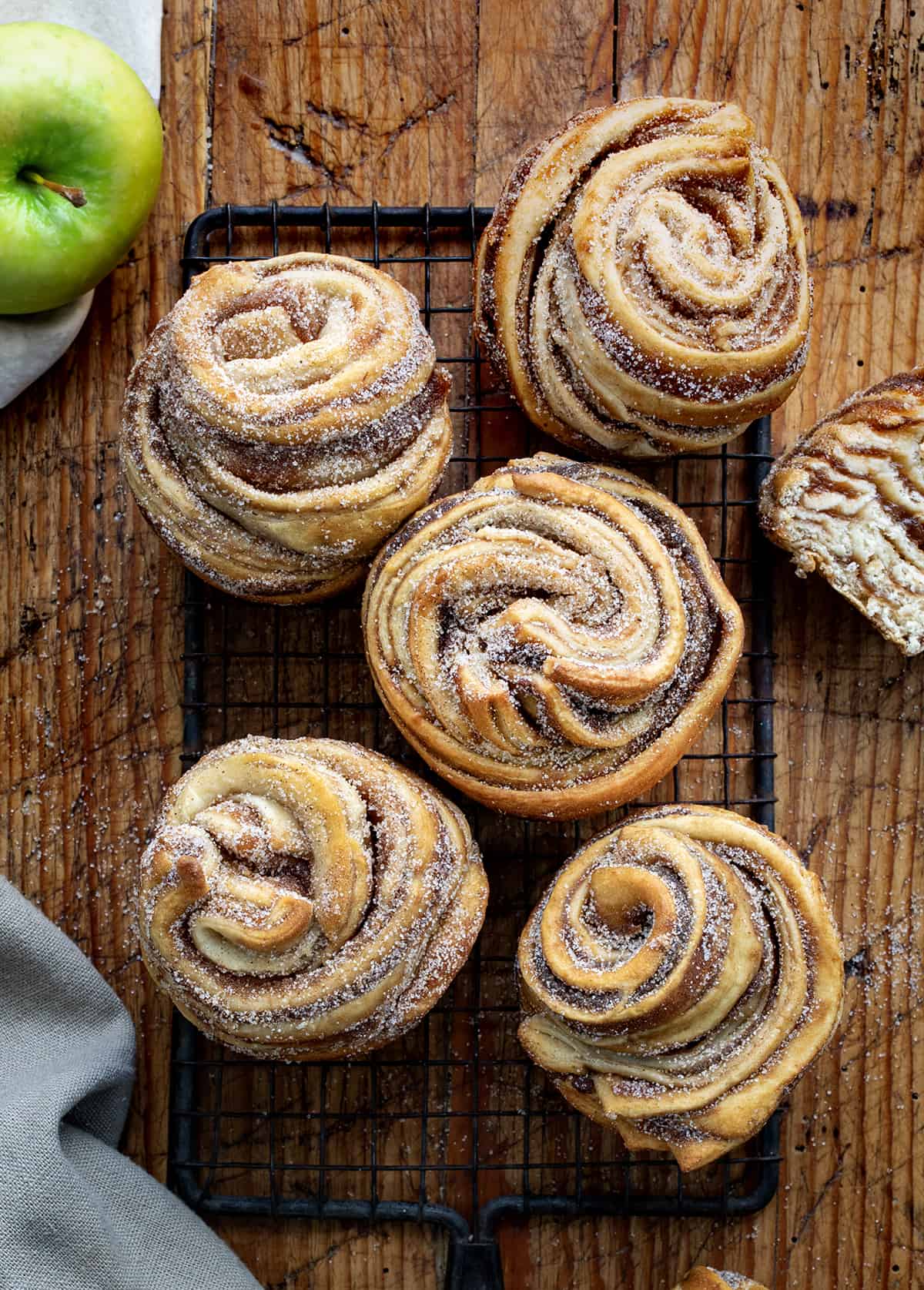 Freshly baked cinnamon rolls with sugar and cinnamon swirl on a cooling rack, wooden table background, perfect for baking and dessert supplies.