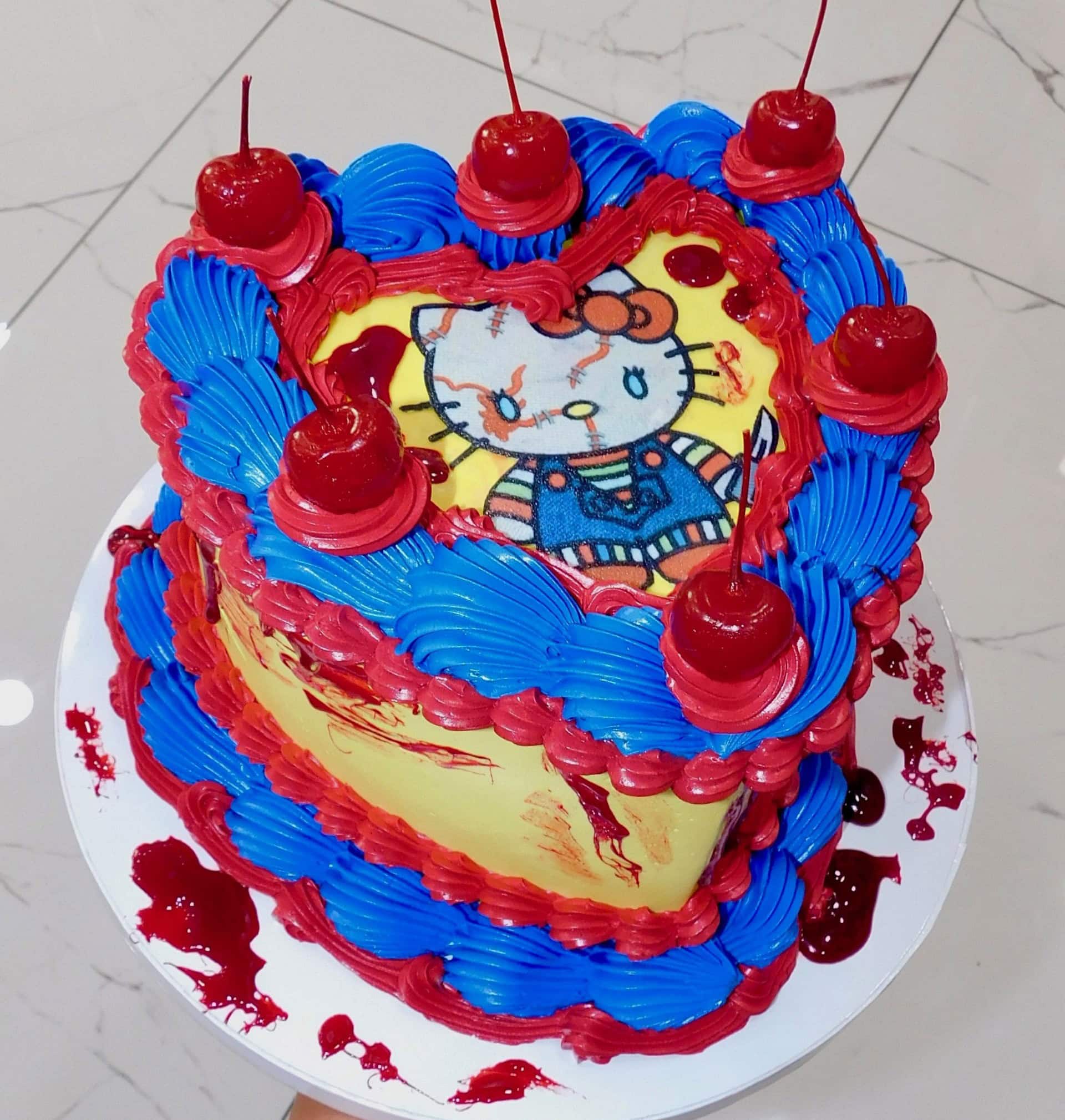 Decorative heart-shaped cake featuring Hello Kitty with red cherries and vibrant blue and red frosting, perfect for celebrations.