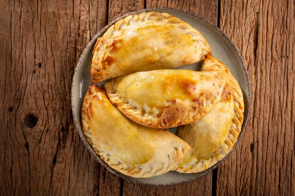 Delicious baked empanadas with melted cheese on top, served on a rustic wooden table, perfect for celebrating Hispanic Heritage Month.