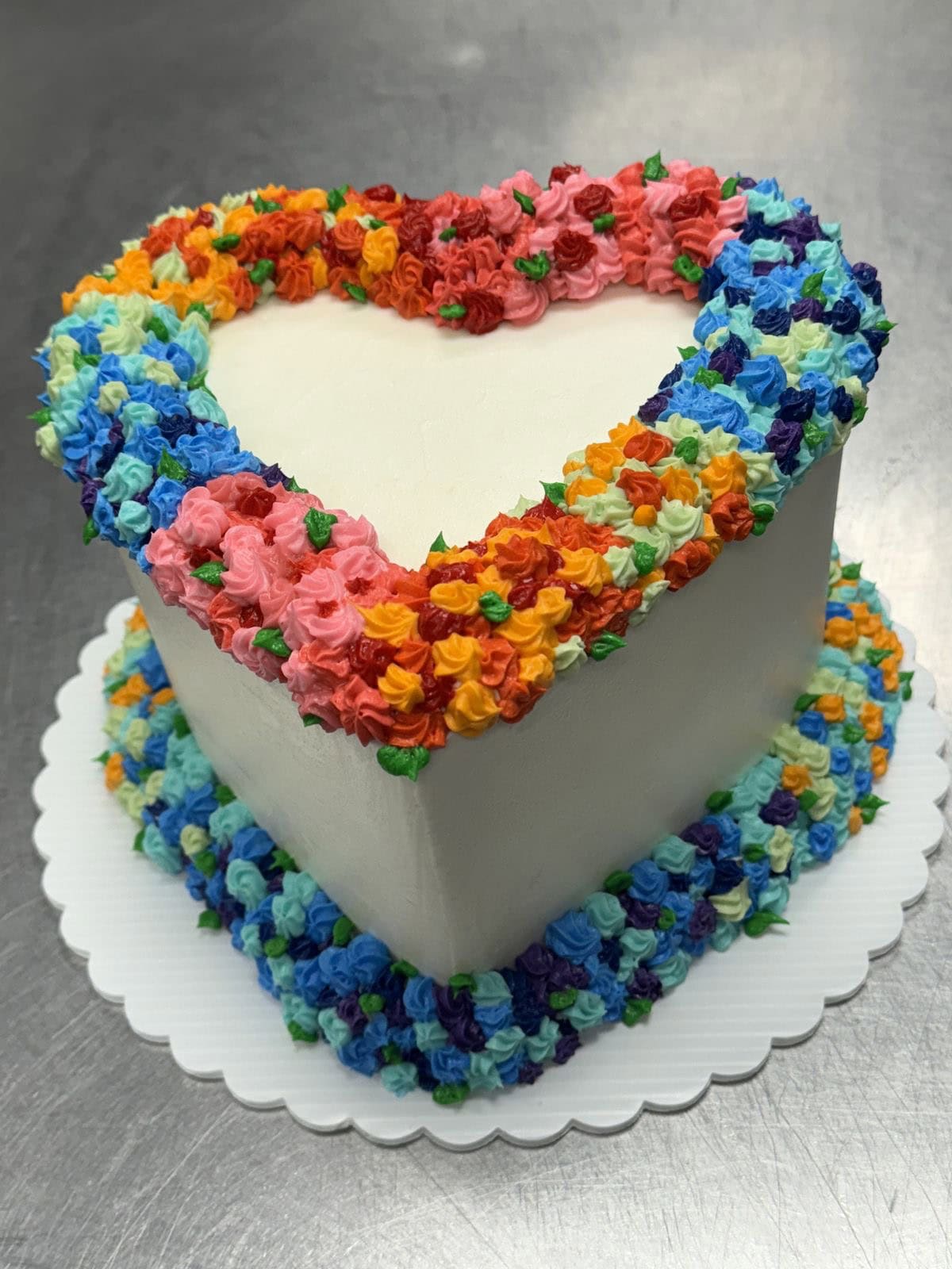 Heart-shaped cake decorated with vibrant multicolored buttercream flowers for celebration or special occasions.