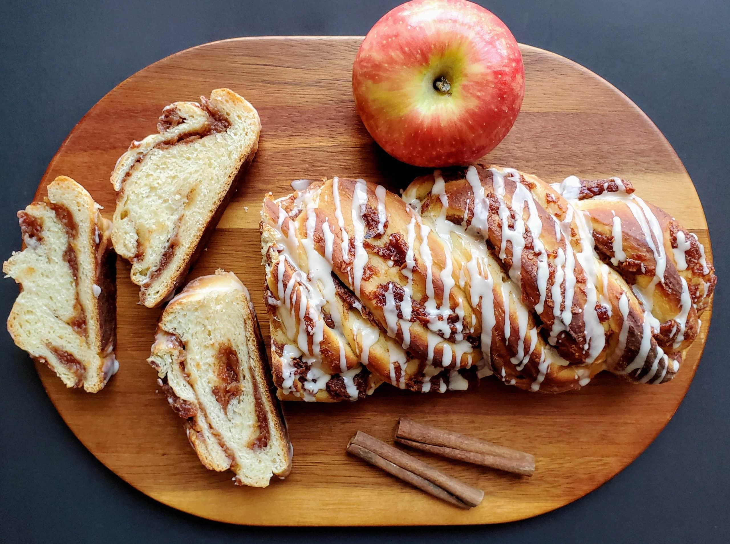 Fresh cinnamon apple twist bread slices with whole apple and cinnamon sticks on a wooden board.