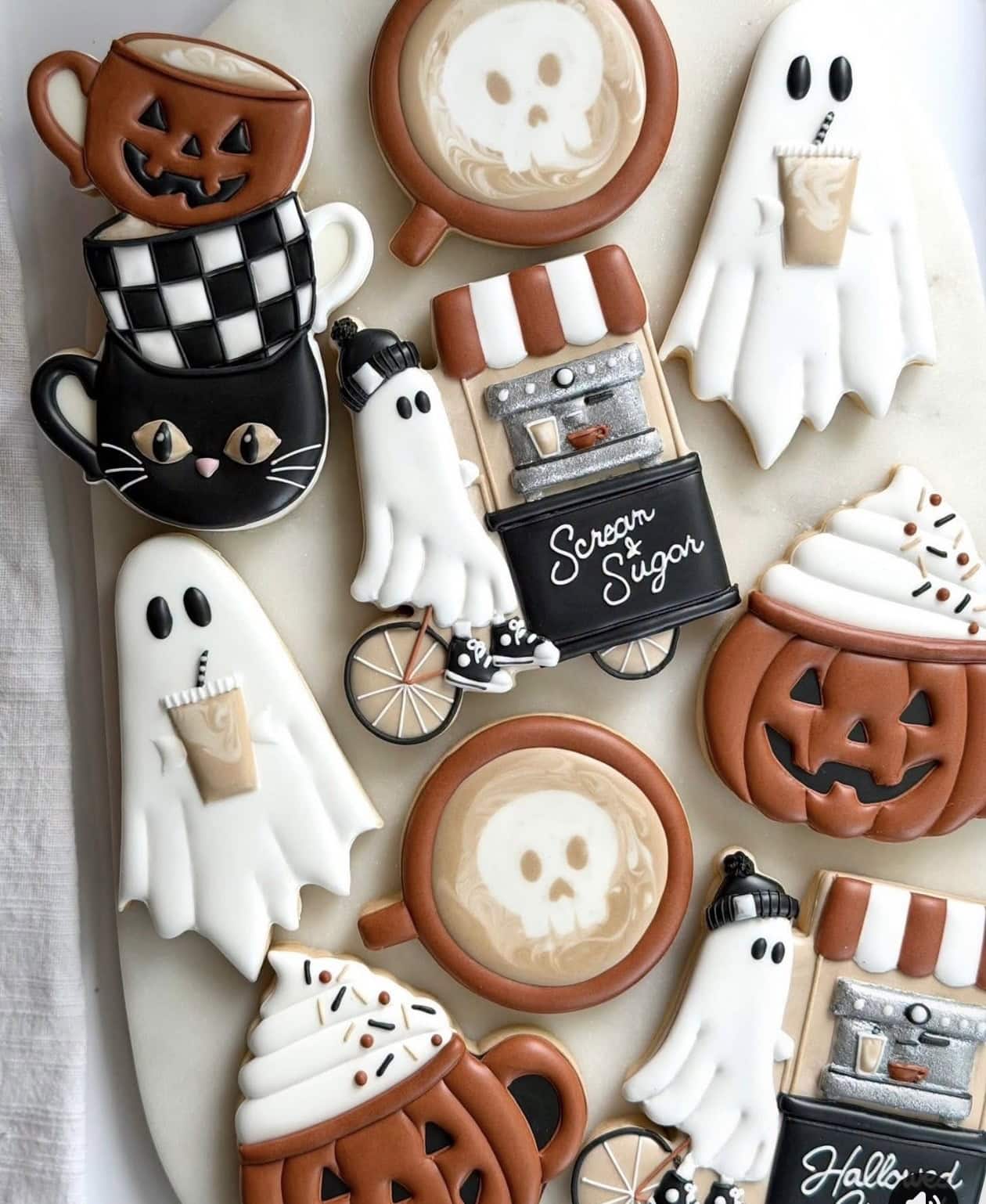 Assorted Halloween-themed cookies including ghosts, pumpkins, and skulls with coffee cups and spooky decorations for festive baking.