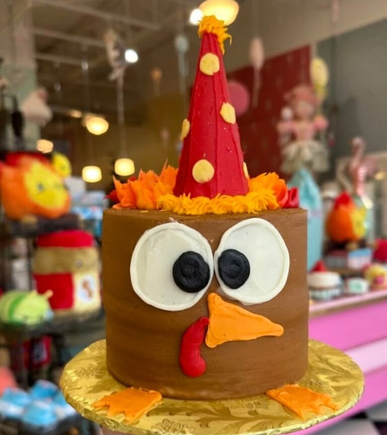 Decorative cake featuring a turkey face with a red party hat, orange beak, and feet, perfect for fall celebrations and themed parties.