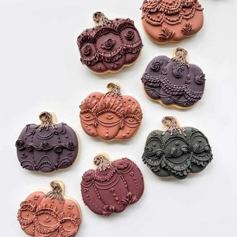 Pumpkin-shaped decorated cookies with intricate icing details in shades of pink, purple, and black, perfect for fall or Halloween celebrations, available at Over the Top Cake Supplies.
