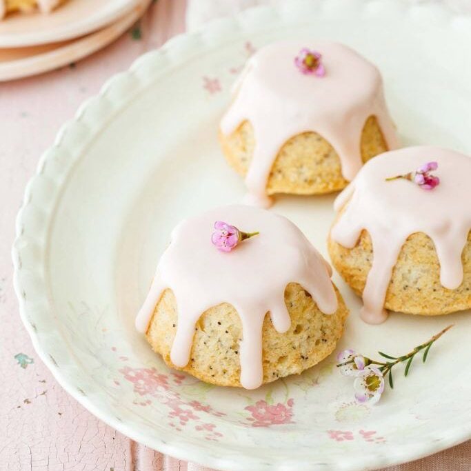 Delicious vanilla cupcakes with pink glaze and floral garnishes on a vintage floral plate, perfect for cake decorating and baking supplies.